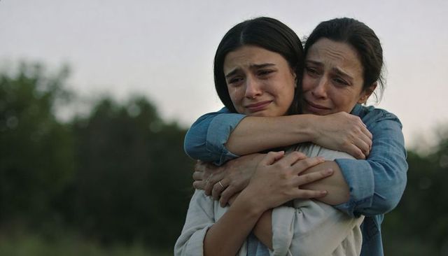 Mother embracing tearful daughter consoling at dusk in grassy field emotional support