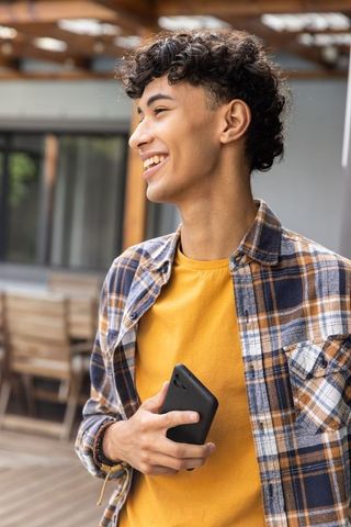 Smiling Young Man Holding Smartphone Outdoors Under Pergola