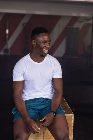 Smiling african american athlete sitting on plyometric box wearing smartwatch post workout