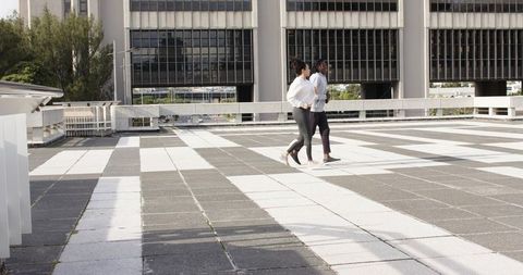Diverse coworkers walking on rooftop terrace across geometric tiled plaza in sunlight
