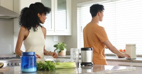 Multiracial couple preparing healthy green smoothie with blender on marble counter