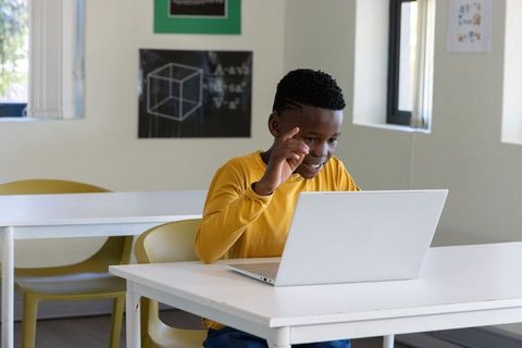 African american boy studying on laptop in classroom, engaged remote learning
