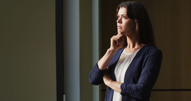Portrait of thoughtful caucasian businesswoman with brown hair standing by window in modern office. business and business people in office concept.
