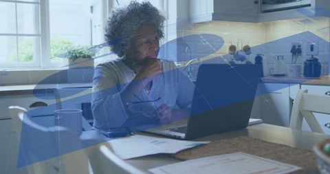 Mature woman working on laptop at kitchen table, digital overlay coding docker tutorial