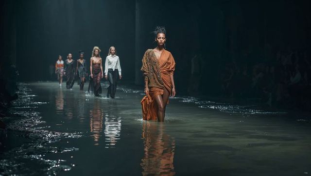 Model in burnt-orange dress on reflective flooded runway