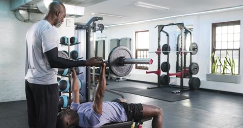 Personal trainer assisting client with bench press in modern gym