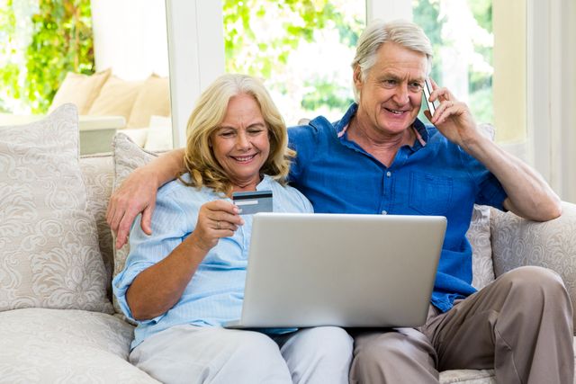 Happy senior couple using laptop while talking on phone at home