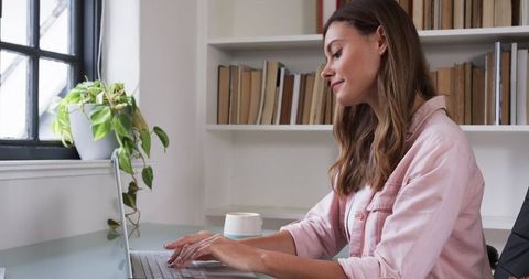 Woman Typing on Laptop in Minimalist Home Office with Coffee