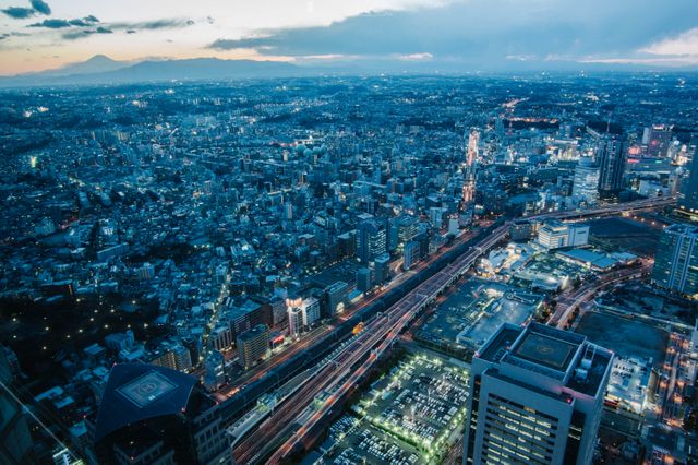 This image showcases a stunning aerial view of Tokyo cityscape at dusk with the silhouette of Mount Fuji in the background. The urban landscape is illuminated with city lights, offering a captivating portrayal of Japan's bustling metropolis. Use this for travel promotions, blogs about Tokyo, urban planning presentations, or articles about Japanese culture.