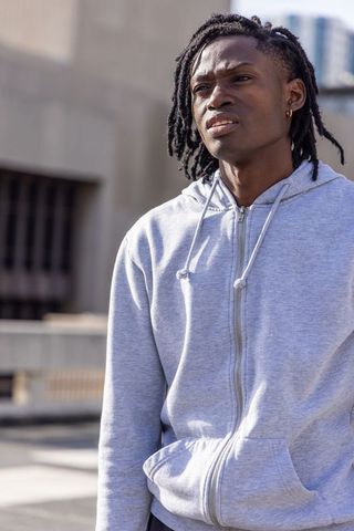 Young man standing on rooftop wearing light gray zip-up hoodie showing hoop earring