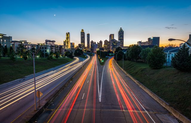 A captivating view of a busy city highway at dusk, featuring vibrant light trails created by moving vehicles. The silhouettes of modern skyscrapers stand tall against the twilight sky, adding to the urban atmosphere. Ideal for use in marketing materials, travel blogs, and articles related to city life and transportation infrastructure.