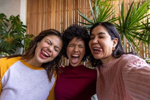 Diverse women making playful faces posing closeup indoors with plants and wooden slats