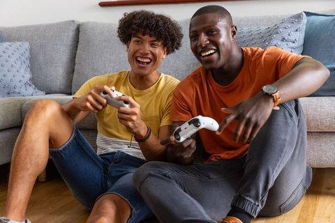 Diverse male friends laughing and playing video games together on living room floor