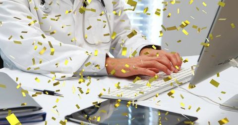 Male doctor typing patient records on desktop keyboard with gold confetti celebration