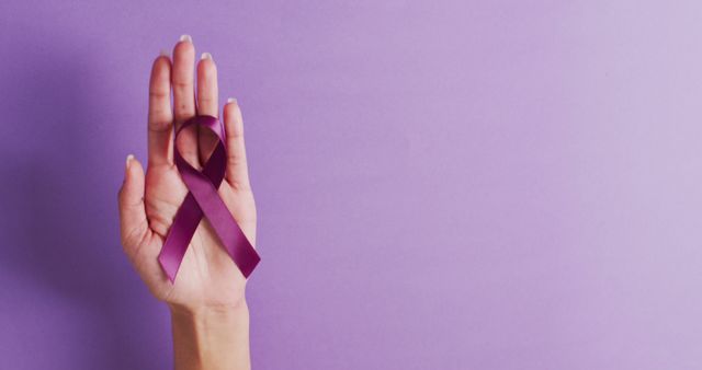 Person raising hand holding purple ribbon symbolizing awareness and support. Ideal for healthcare campaigns, charity events, and promotional materials aimed at highlighting important health issues, particularly related to cancer awareness or domestic violence prevention.