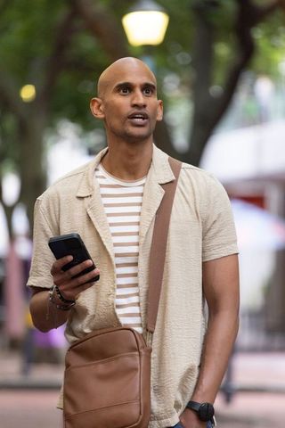 African man walking urban street at dusk holding smartphone and leather crossbody bag