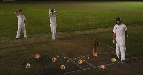 Night cricket players standing near wicket with scattered emoji reactions on grass pitch
