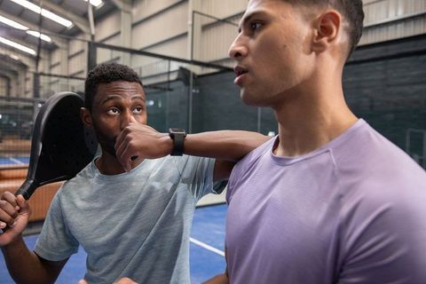 Two male players pausing on indoor paddle court wearing athletic jerseys and wristwatch