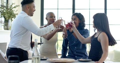 Diverse friends toasting at modern dining table during bright indoor celebration
