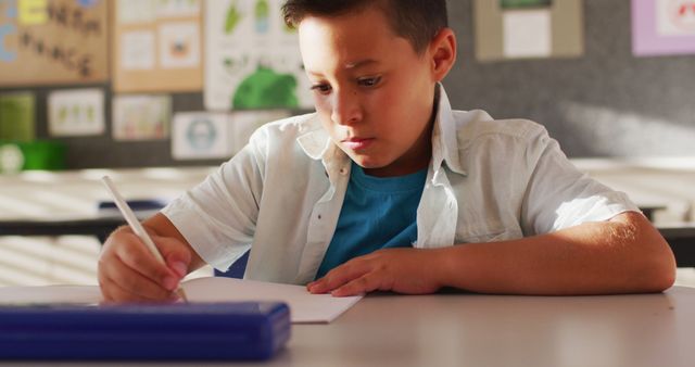 Portrait of biracial schoolboy sitting in class, making notes, looking at camera. children at primary school in summer.