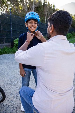 Father Adjusting Son's Bike Helmet Outdoors for Safety