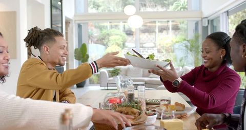 Diverse Friends Passing Salad Sharing Meal at Bright Modern Open-Plan Dining Table