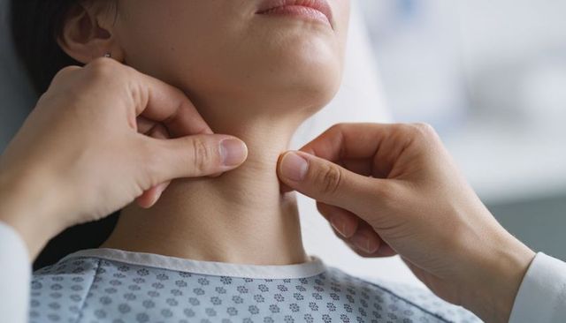 Physician palpating thyroid during neck examination of woman wearing medical gown