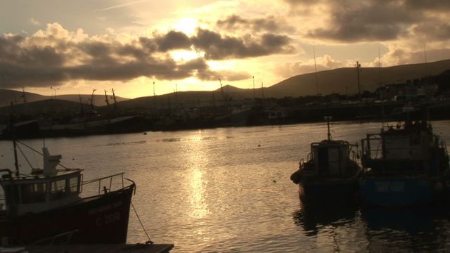 Stunning evening scene with sun descending over the Kerry coast, perfect for use in travel magazines, calendar photos, tourism advertisements, and serene landscape compilations. The calm water and moored boats amplify the peaceful and tranquil atmosphere.