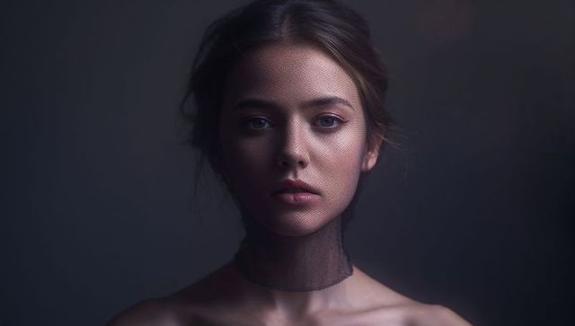 Gazing young woman wearing sheer black net choker, bare shoulders, moody sidelight portrait