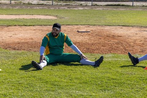 Stretching baseball player warming up on grass at sunny ballpark preparing for game