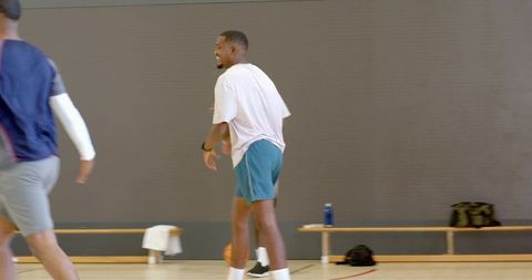 Casual basketball player smiling and defending on indoor court with bench and gear