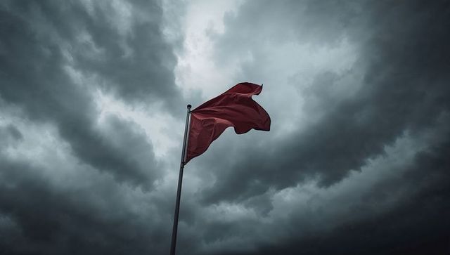 Waving crimson flag on tall pole beneath dark storm clouds conveying danger and warning