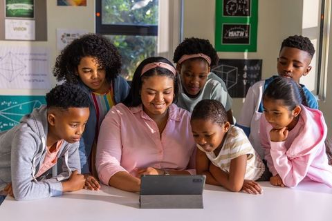 African american teacher guiding diverse young students on tablet, smiling and learning