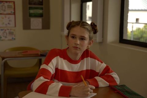 Young female student writing at classroom desk in red striped sweater focused on schoolwork