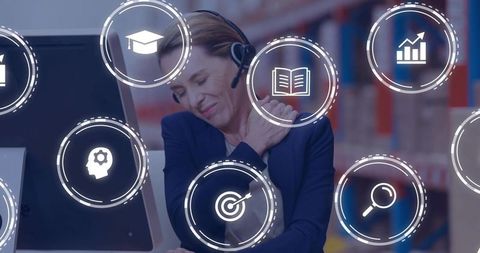 Mature woman rubbing shoulder wearing headset leaning at monitor with business icons overlay