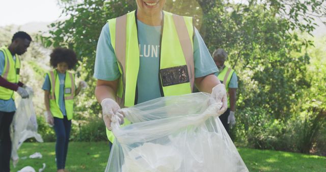 Volunteers wearing high-visibility vests and gloves are cleaning a park by collecting trash. This image is ideal for use in content related to community service, environmental conservation campaigns, teamwork, and social responsibility initiatives.