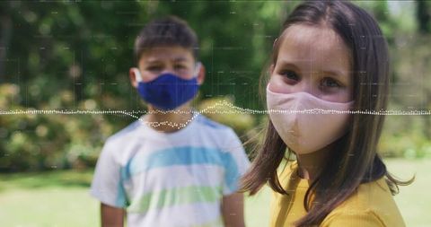 Sunlit children wearing face masks with digital soundwave overlay in garden