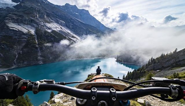 Riding motorcycle overlooking turquoise alpine lake, mist drifting across mountain cliffs