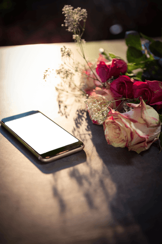 Transparent smartphone lying next to elegant blooming flowers