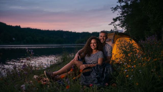 Couple Cuddling at Lakeside Campsite at Dusk with Warm Tent Glow and Wildflowers