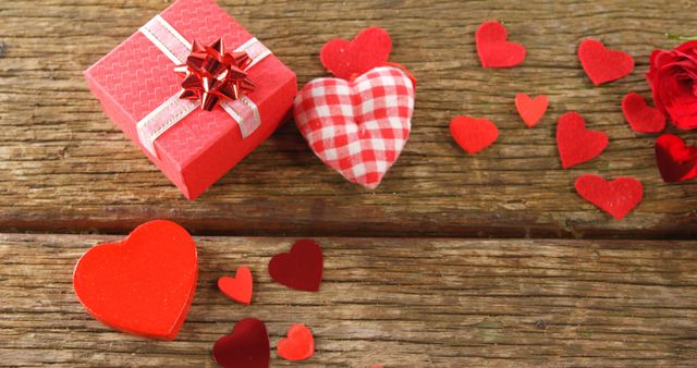 A red gift box and various heart shapes are scattered on a wooden surface, symbolizing romance and love, with copy space. Perfect for Valentine's Day or romantic occasions, the image evokes feelings of affection and celebration.