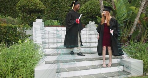 Graduates descending garden steps holding diploma scrolls red ribbons celebrating success