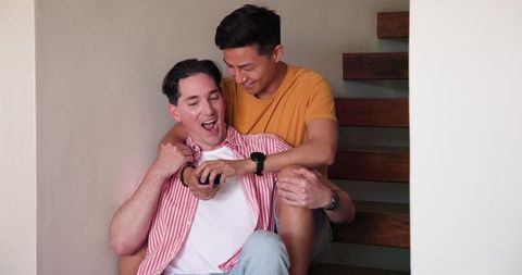 Joyful Diverse Male Couple Bonding on Wooden Stairs