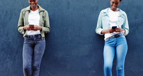 Smiling Twins with Smartphones on Urban Sidewalk