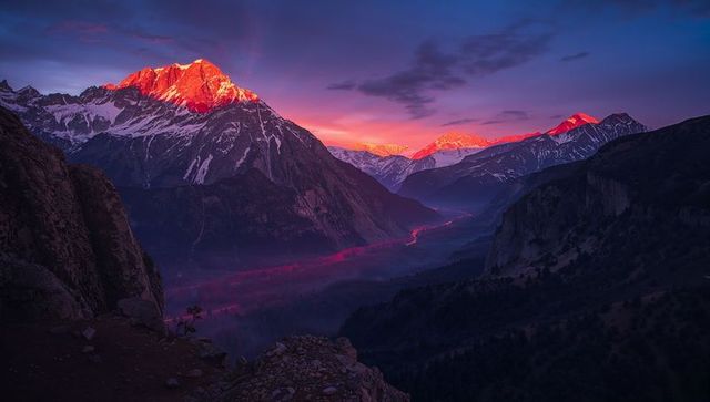 Alpenglow bathing snow-capped mountain peaks over misty alpine valley at sunset with red river