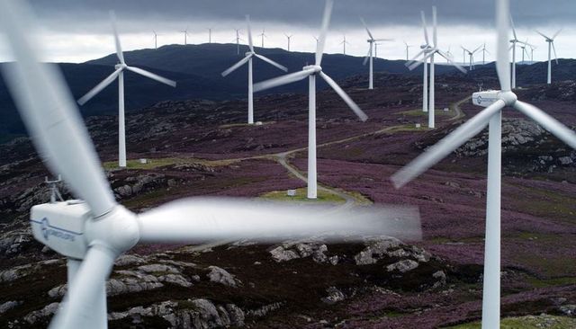 Rotating wind turbines powering moorland heather with winding access road and motion blur