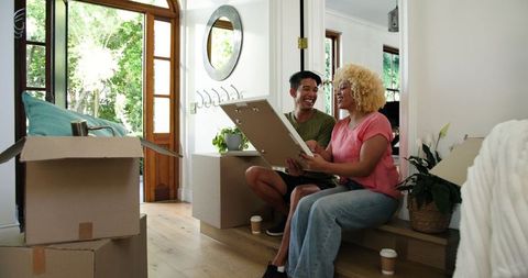 Smiling couple unpacking picture frame in new home's bright hallway