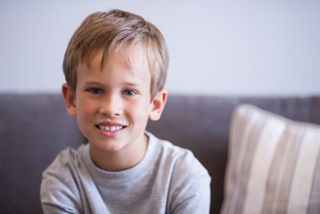Young boy with a cheerful expression sitting on a sofa in a hospital setting. Ideal for use in healthcare, pediatric care, and family-oriented content. Can be used to depict positive healthcare experiences, child-friendly environments, and patient comfort.