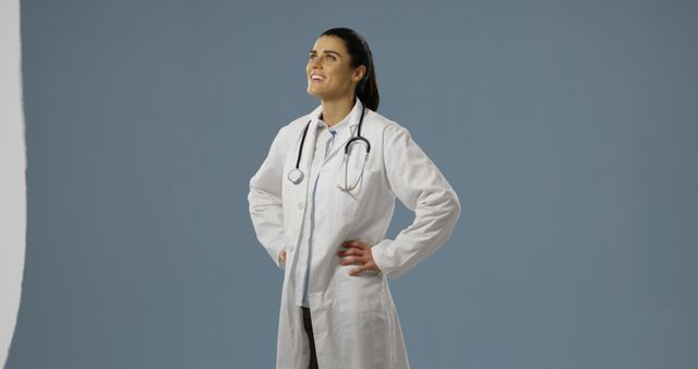 Confident female doctor stands proudly in her white coat, with copy space. Her professional attire and stethoscope signify her medical expertise.