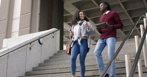 Diverse coworkers walking down concrete stairs chatting and using phone and tablet in city